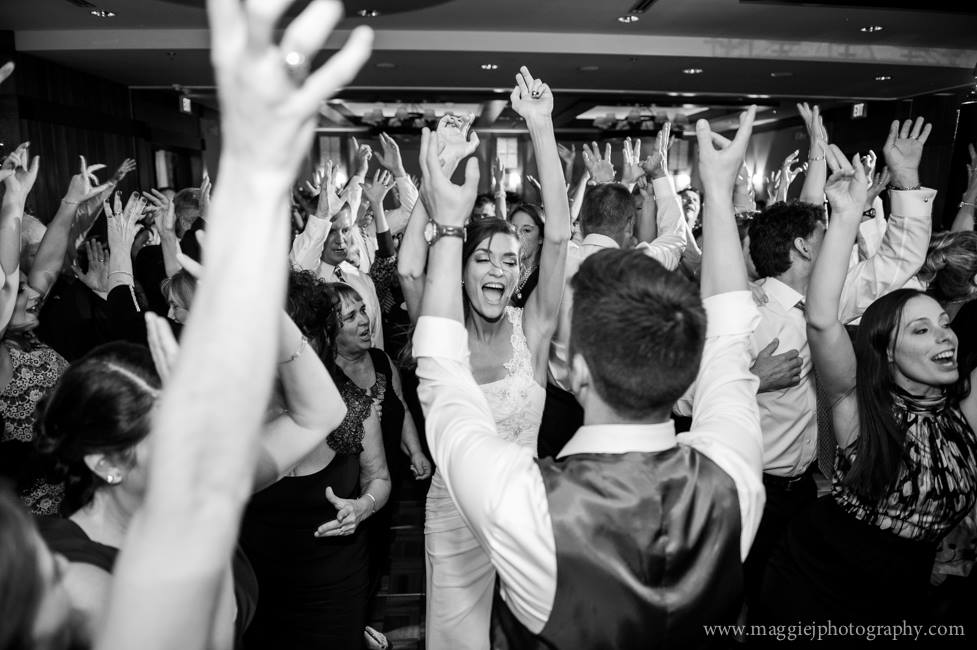 A bride and groom dancing with their arms in the air at their wedding reception